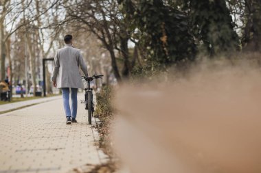 Sıradan bir iş adamı şehir kaldırımında bisikletinin yanında yürürken etrafını seyrediyor..