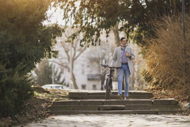 Sıradan bir iş adamı bisikletle şehir parkında bir dizi taş basamaktan aşağı iniyor ve güneşli bir günde kahvenin tadını çıkarıyor..