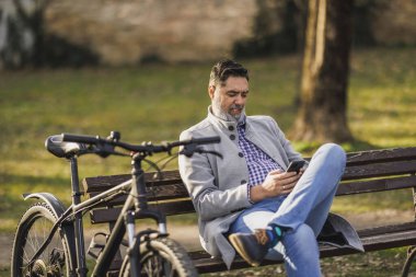 Sıradan bir iş adamı, bisikletini yanındaki bankta, cep telefonuna kaptırmış, daktilo ve kaydırma ile mola verir..
