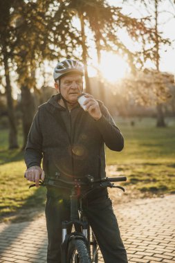 Son sınıftan bir adam bisikletin yanında elinde tek kullanımlık kahveyle bisiklete binmekten zevk alıyor..