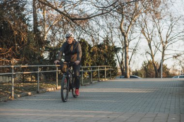 Kask takan son sınıf öğrencisi şehir parkında bisiklet sürüyor..