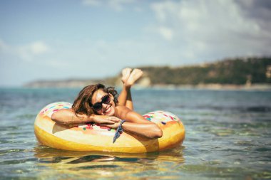 Güzel genç bir kadın deniz suyunda şişme bir yüzüğün üzerinde yüzüyor ve yaz tatilinin tadını çıkarıyor..
