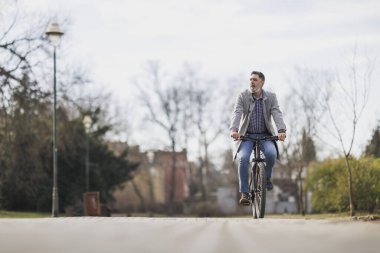 Sakallı sıradan bir iş adamı şehir parkında kaldırımdan aşağı dağ bisikleti sürüyor..