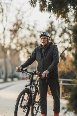 Yaşlı bir adam şehir kaldırımında bisikletinin yanında durur, etrafına bakar ve bir sonraki hedefini planlar ya da bir arkadaşını bekler..
