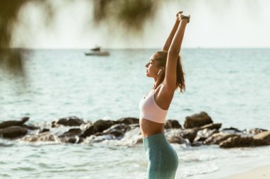 Genç bir kadın okyanus kenarında kollarını uzatıyordu. Yaz tatilinde bir plaj kenarında yoga antrenmanı yapıyor..