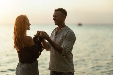 Bir adam ve bir kadın, boş bir okyanus sahilinde günbatımının tadını çıkarıyorlar. Birbirlerine bakıp mutlu bir şekilde gülümsüyorlar..