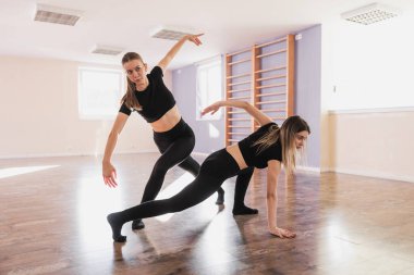 İki genç kadın, modern bale hareketlerini parlak bir dans stüdyosunda yapıyorlar.. 