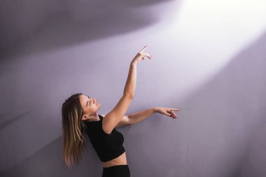 Siyah spor kıyafetli genç bir kadın modern bale çalışmasını bir dans stüdyosunda yapıyor..