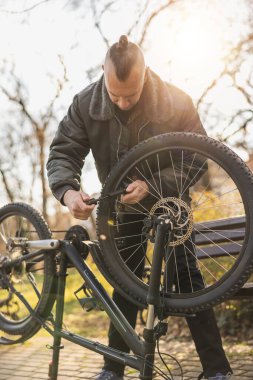 Orta yaşlı bir adam, şehir parkına gitmeden önce devrilmiş bisikletinin lastiğini şişiriyor..
