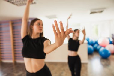 İki genç kadın parlak bir fitness stüdyosunda dans figürleri çalışıyor. Uzatılmış bir ele yakın çekim.