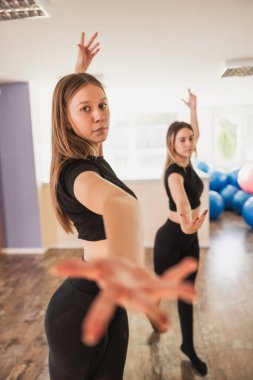 İki genç kadın, modern bale hareketlerini parlak bir dans stüdyosunda yapıyorlar..