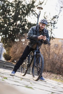 Orta yaşlı bir adam şehir parkında bir bisikletin tepesinde oturuyor, internette geziniyor ya da akıllı telefonundan mesaj yolluyor..