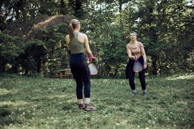 İki bayan arkadaş, doğadaki ormanın yakınındaki çayırda eğlenceli badminton oynuyorlar. Hafta sonu aktiviteleri. Aile eğlencesi.