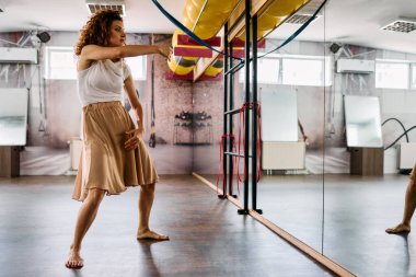 Stüdyoda kıvırcık saçlı, salsa yapan ve aynaya çıplak ayakla bakan güzel bir kadın..