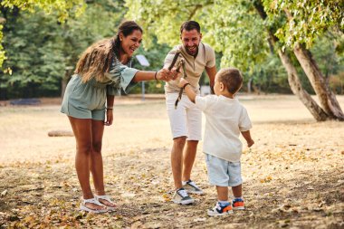 Aile parktaki ağaç dallarıyla oynuyor. 