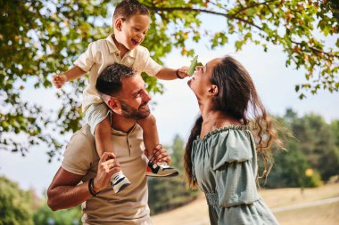 Oyuncu aile eğlenirken, baba oğlunu omuzlarında tutuyor..