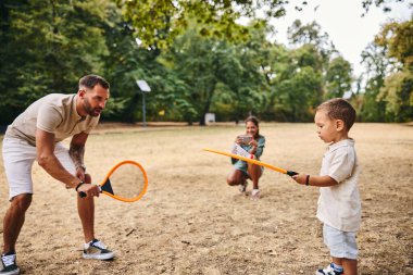 Anne onların doğada fotoğraflarını çekerken baba ve oğul badminton oynuyor..