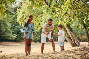 Aile parktaki ağaç dallarıyla oynuyor. 