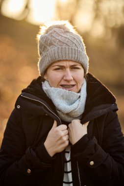 Bir kadın ceketinde şapka ve atkıyla parkta üşür. 