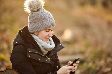 Parkta rahat rahat otururken telefonunu kullanan gülümseyen bir kadın.