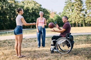 Bir aile, tekerlekli sandalyedeki bir adamla açık havada basketbol oynamaktan zevk alır..