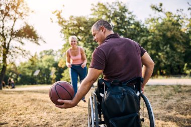 Aile, tekerlekli sandalyedeki adamla basketbol oynarken parkta eğleniyor..