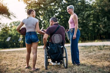 Mutlu aile parkta yürüyor ve tekerlekli sandalyedeki adamla konuşuyor.. 