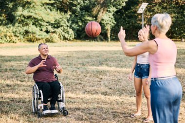 Bir aile, tekerlekli sandalyedeki bir adamla açık havada basketbol oynamaktan zevk alır..