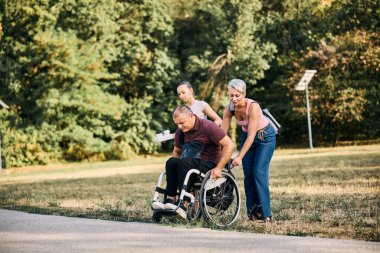 Tekerlekli sandalyedeki bir kullanıcıya yardım eden bir aile parkta günün tadını çıkarıyor..