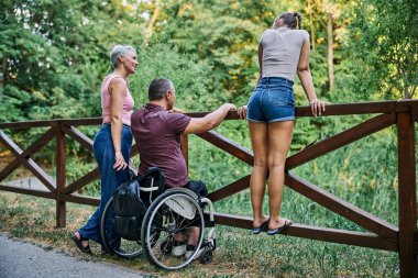 Bir aile, yemyeşil bir parkta güneşli bir günün tadını çıkarır. Bir üye tekerlekli sandalyede.. 