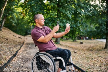Tekerlekli sandalyedeki bir adam yemyeşil bir parkta huzur ve özgürlüğe kucak açan bir yürüyüşün tadını çıkarır..