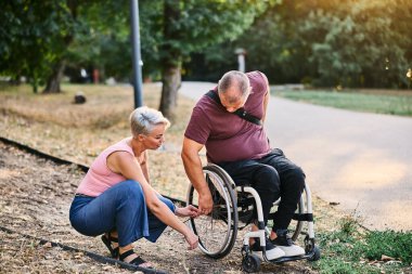 Bir kadın, tekerlekli sandalyedeki bir adama parkta bir patikada yol göstermesine yardım eder..