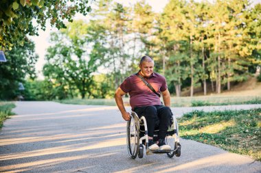 Tekerlekli sandalyedeki bir adam yemyeşil ağaçlarla çevrili huzurlu bir park yolunu keşfediyor.. 