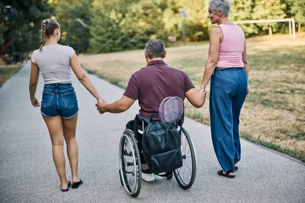 Doğada, tekerlekli sandalyedeki adamlarla yürüyen aile manzarası.. 