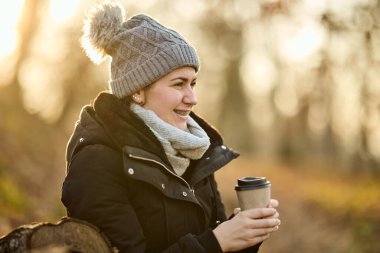Gülümseyen bir kadın parkta rahat rahat otururken kahvesini içiyor.. 