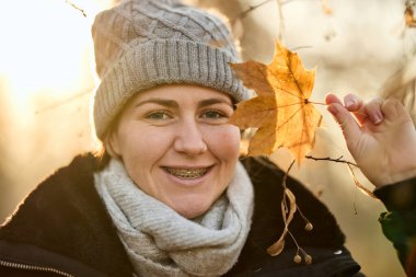 Genç bir kadının portresi elinde bir yaprak tutuyor ve dışarıda kameraya gülümsüyor..