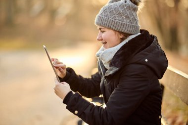 Genç bir kadın, sonbahar gününün keyfini çıkarırken sosyal medyada içeriklerini tarayan tablet ekranına odaklanıyor..