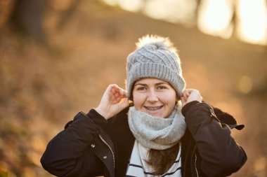 Parkta durup kameraya bakan, şapka ve eşarp takan, gülümseyen bir kadın.. 