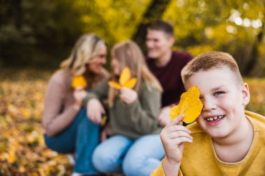 Dört kişilik bir aile, sonbahar parkında yapraklı poz veriyor ve onlarla oynuyor.. 