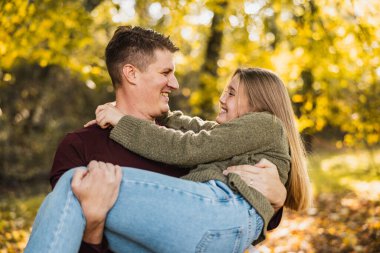 Gülümseyen baba-kız parkta eğlenirken baba kızını sonbahar parkında tutuyor.. 