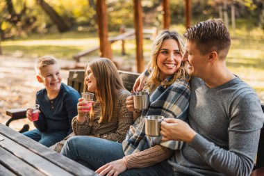 Aile parkta güzel bir sonbahar ortamında bankta oturur ve sıcak tişört içer..