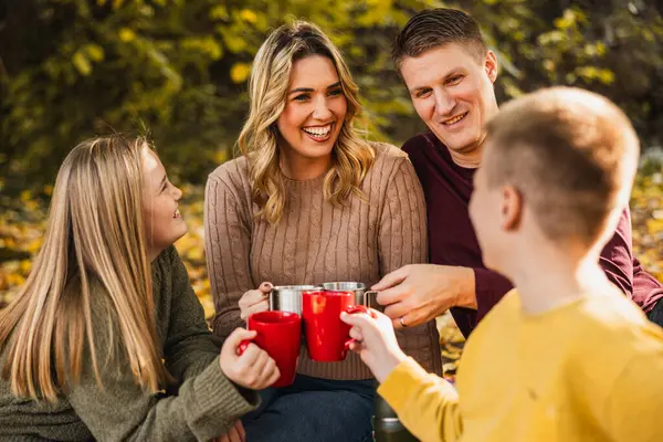 Dört kişilik aile, güzel bir sonbahar gününde sıcak çay içerken parkta piknik yapıyorlar.. 