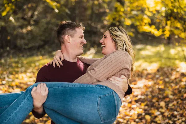 Neşeli bir çift, sonbahar renkleriyle dolu güneşli bir parkta kucaklaşıyor.. 