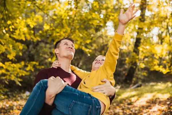 Gülümseyen baba ve oğul parkta eğlenirken baba oğlunu sonbahar parkında tutuyor.. 