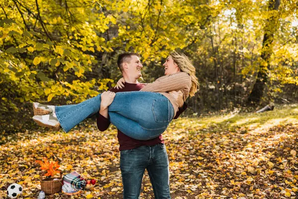 Neşeli bir çift, sonbahar renkleriyle dolu güneşli bir parkta kucaklaşıyor.. 