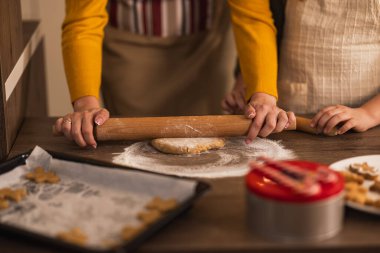 Sıcak bir mutfak ortamında kurabiye için hamuru yuvarlayan bir anne ve çocuğun elleri sıcak ve keyifli bir pişirme deneyimi yaratıyor..