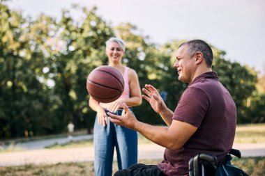 Aile, tekerlekli sandalyedeki adamla basketbol oynarken parkta eğleniyor..