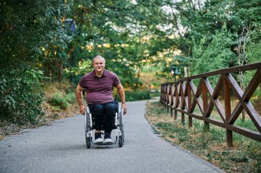 Tekerlekli sandalyedeki bir adam ahşap bir çitin yanında doğanın manzarasının tadını çıkarır.