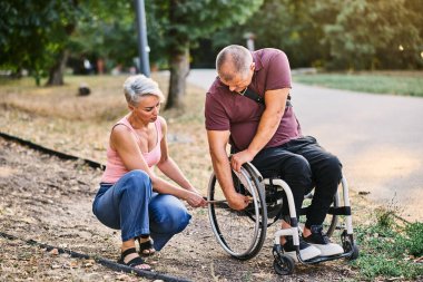 Bir kadın, tekerlekli sandalyedeki bir adama parkta bir patikada yol göstermesine yardım eder..
