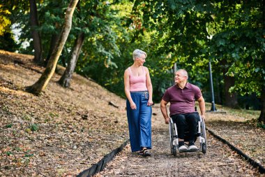 Bir çift, refakatçilik ve kapsayıcılığın altını çizerek, lüks bir parkta sakin bir şekilde yürümekten zevk alır..